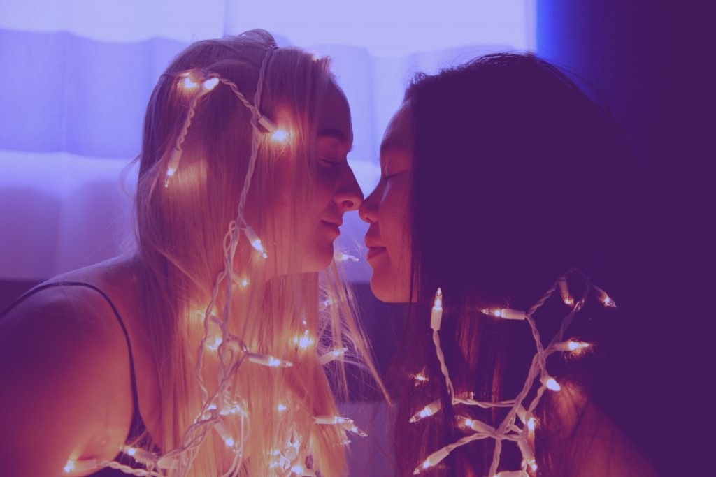 Sex Quirks - two women about to engage in a kiss, both wearing string lights