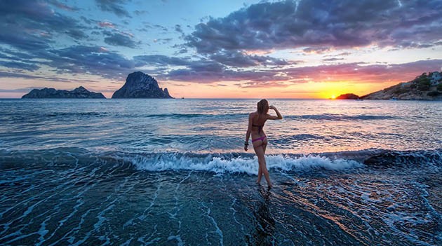 sexy getaway - woman in bathing suit staring at sunset on beach